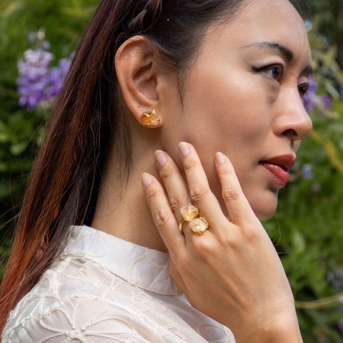 Woman wearing gold earrings and ring with a blurred natural background
