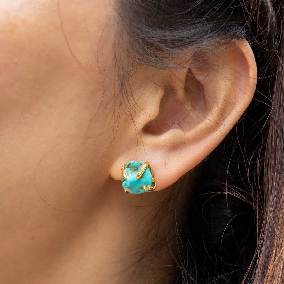Close-up of an ear wearing a turquoise earring with gold accents.