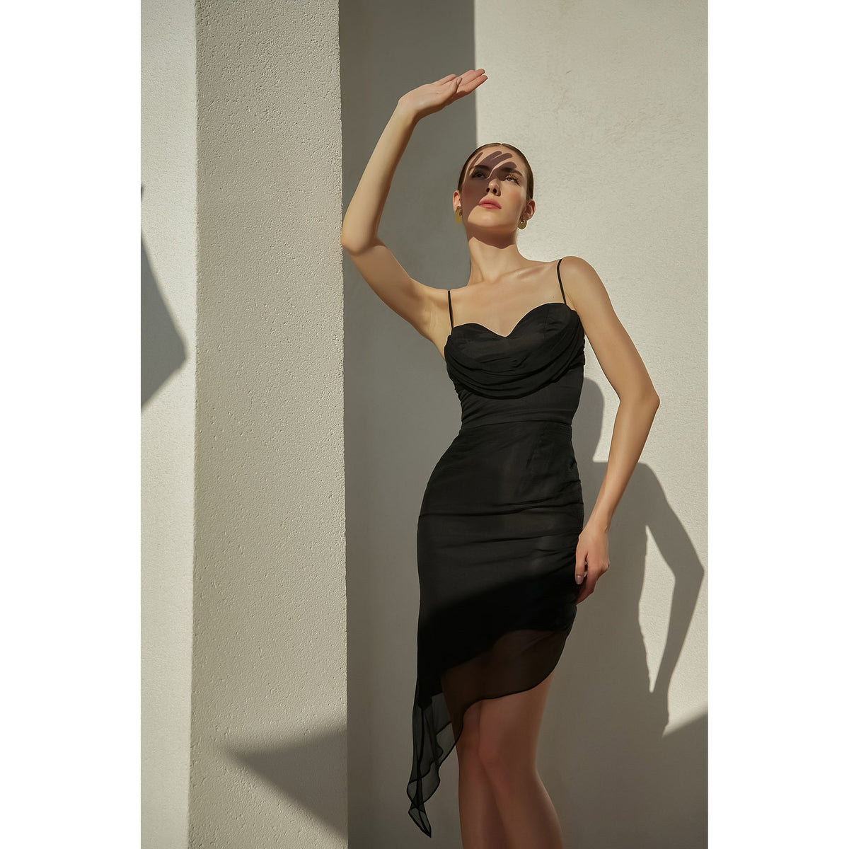 Woman in a black dress standing against a light wall