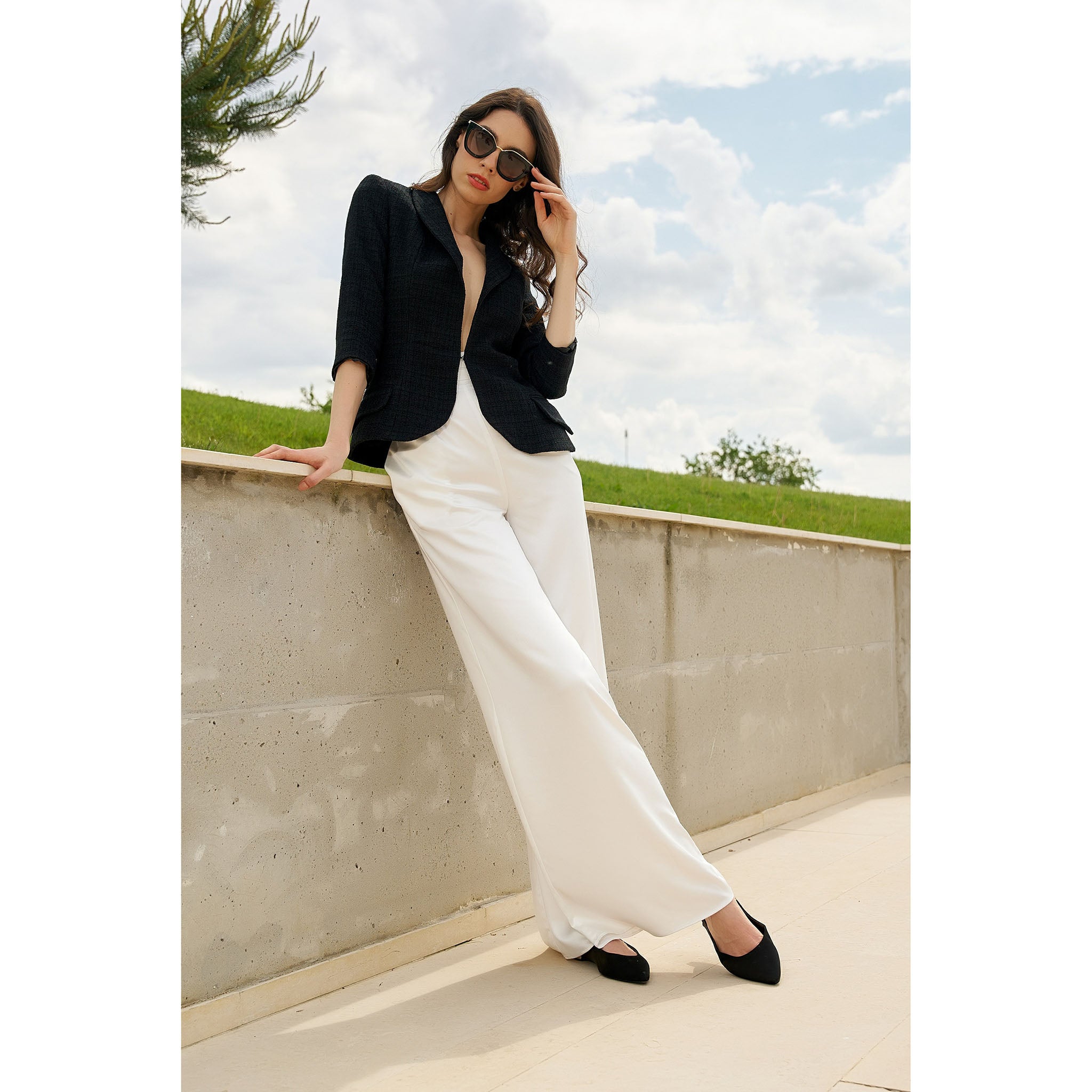 Woman in black top and white pants standing on a rooftop with a cloudy sky background