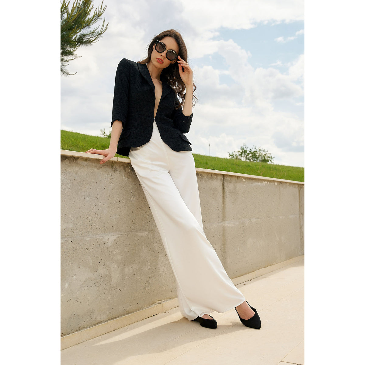 Woman in black top and white pants standing on a rooftop with a cloudy sky background