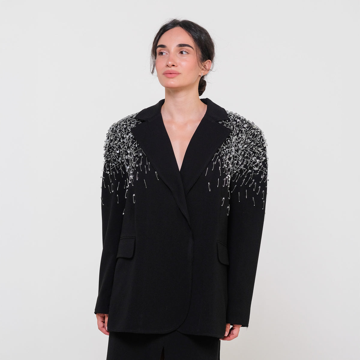 Person wearing a black blazer with silver embellishments on a white background