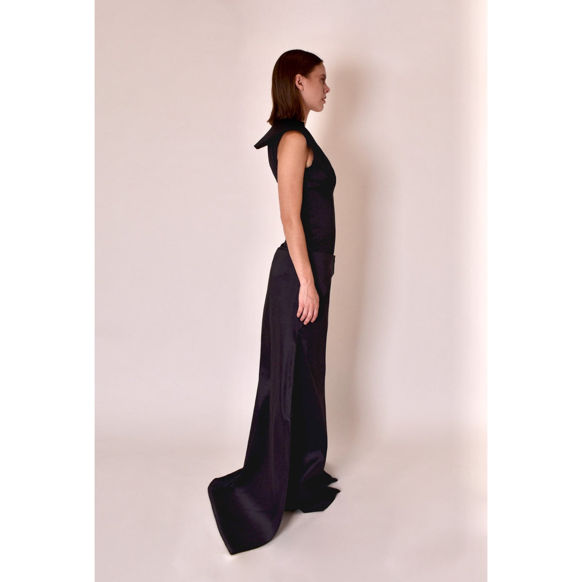 Woman wearing a black evening gown with a bow detail on a plain background