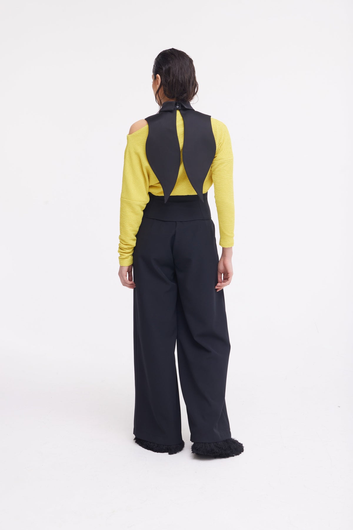 A person faces away, wearing a yellow long-sleeve cutout-shoulder top and JULIA ALLERT Buttoned Corset-Waist Black Tailored Trousers. A unique black collar with two pointed panels drapes down the back, set against a plain white background.