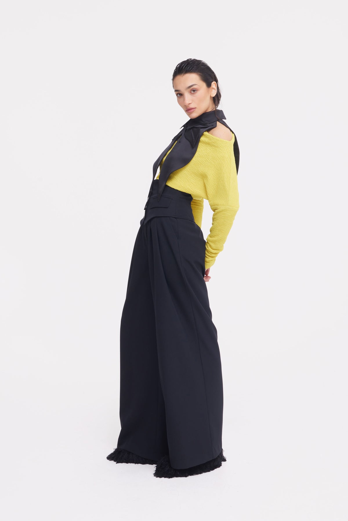 A woman poses confidently on a white background, wearing JULIA ALLERT Buttoned Corset-Waist Black Tailored Trousers paired with a yellow long-sleeve top and a black neck scarf, leaning slightly as she looks at the camera.