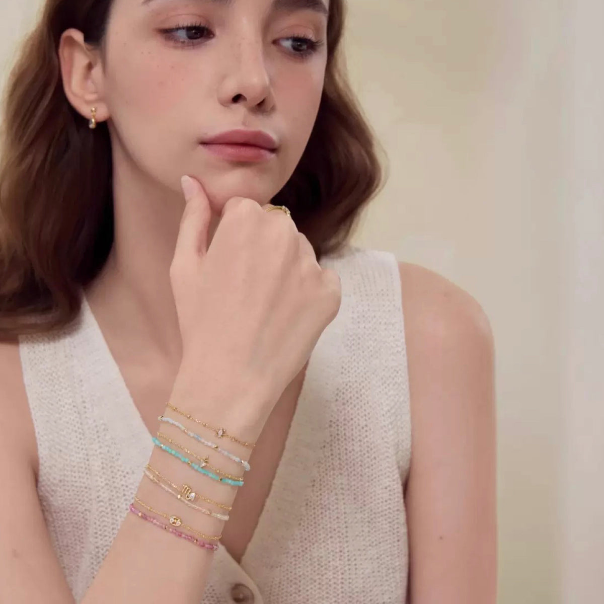 Woman wearing multiple bracelets on her wrist with a neutral background