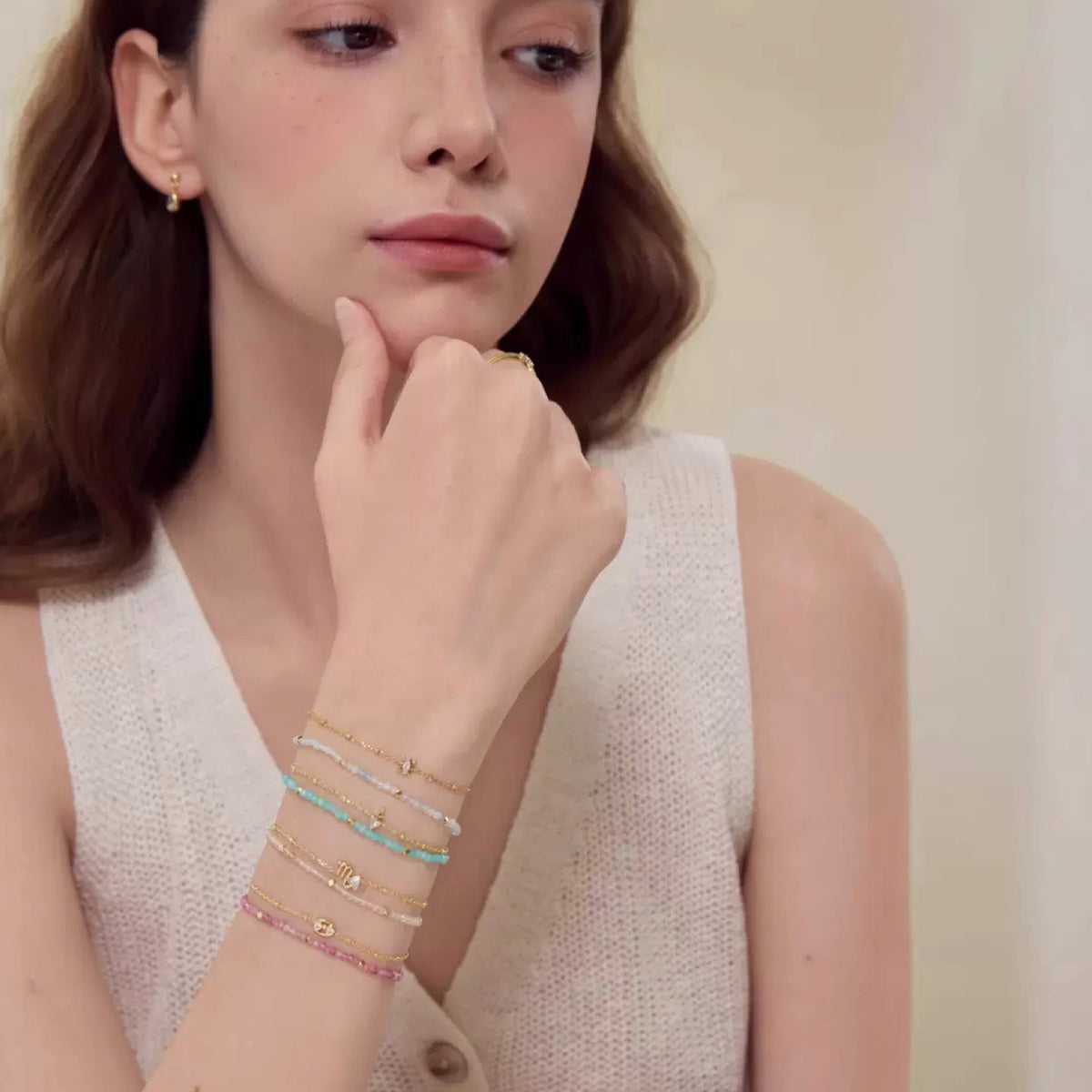 Woman wearing multiple bracelets on her wrist with a neutral background