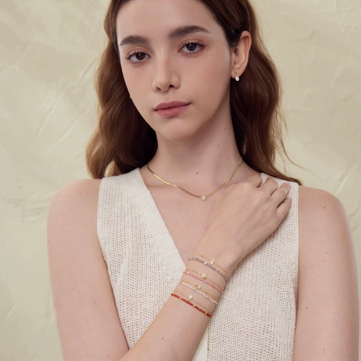 Woman wearing gold necklaces and bracelets on a beige background