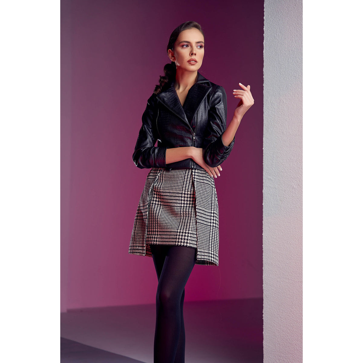 Woman wearing a black leather jacket and plaid skirt against a purple background