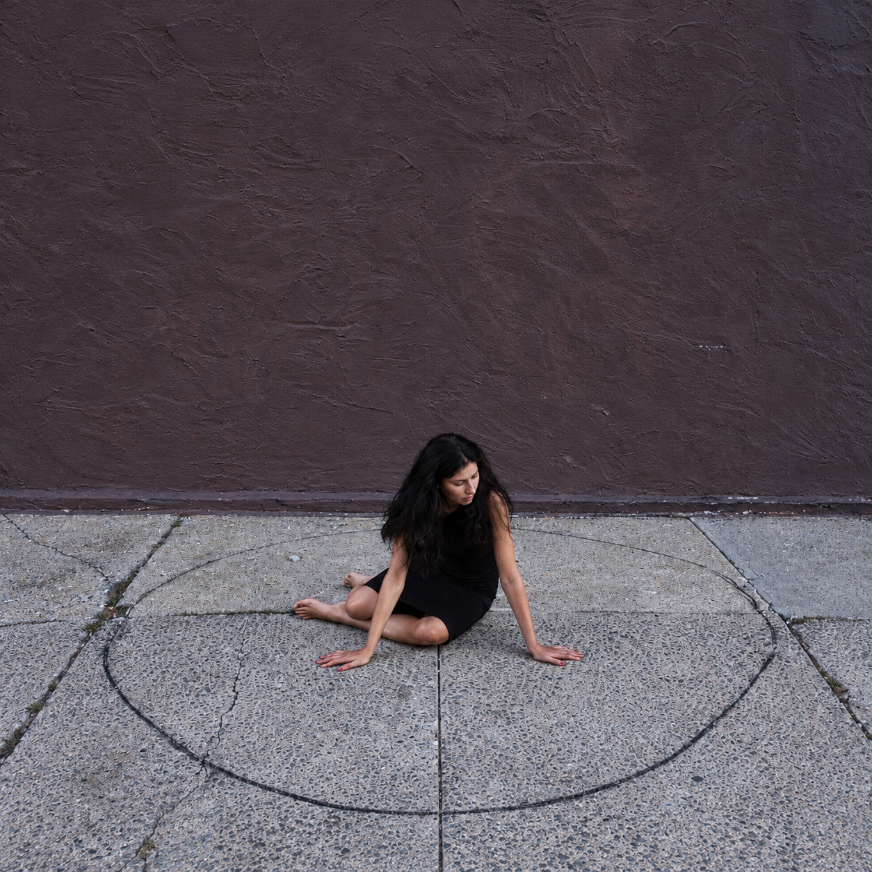 ALSU SHARM Circle II, fine art photography of a woman in a black dress sitting inside a drawn circle on a sidewalk in front of a brown wall, limited edition, buy contemporary art at DOORS NYC