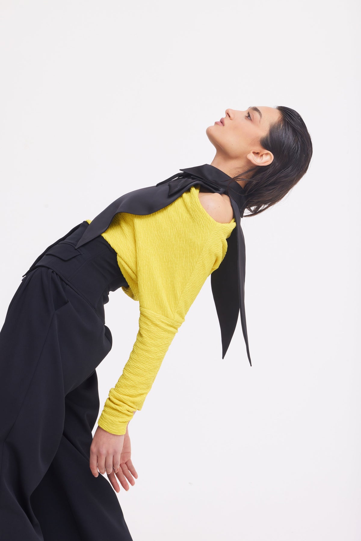Wearing JULIA ALLERT’s Buttoned Corset-Waist Black Tailored Trousers and a yellow top, a person leans back with eyes closed and head tilted up, draped in a black scarf, set against a plain white background.