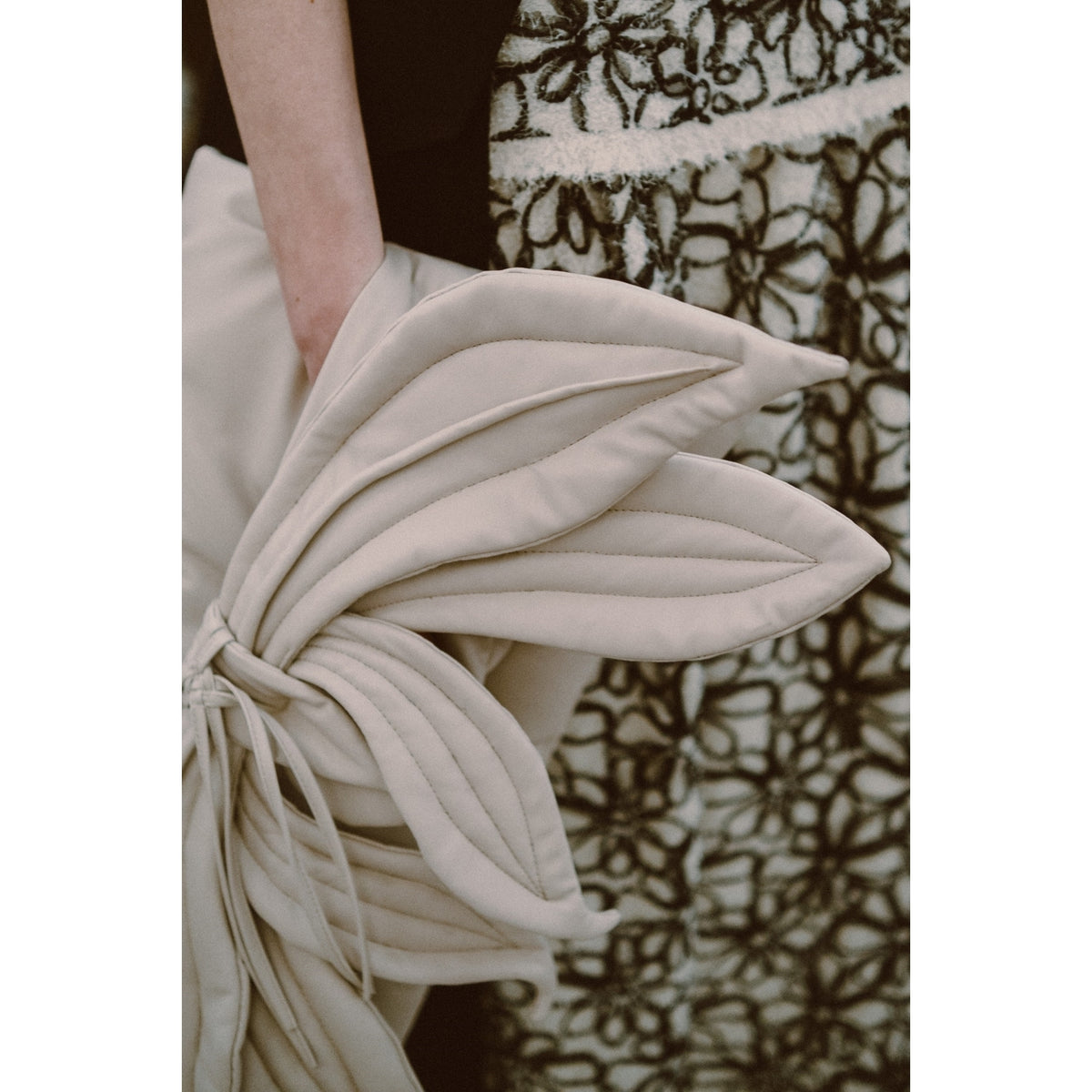 A person holds the JULIA ALLERT Petal Faux Leather Evening Clutch Bag in ecru, its overlapping leaf shape complementing a black and white floral skirt—creating a refined, neutral look in line with Julia Allert’s sophisticated style.
