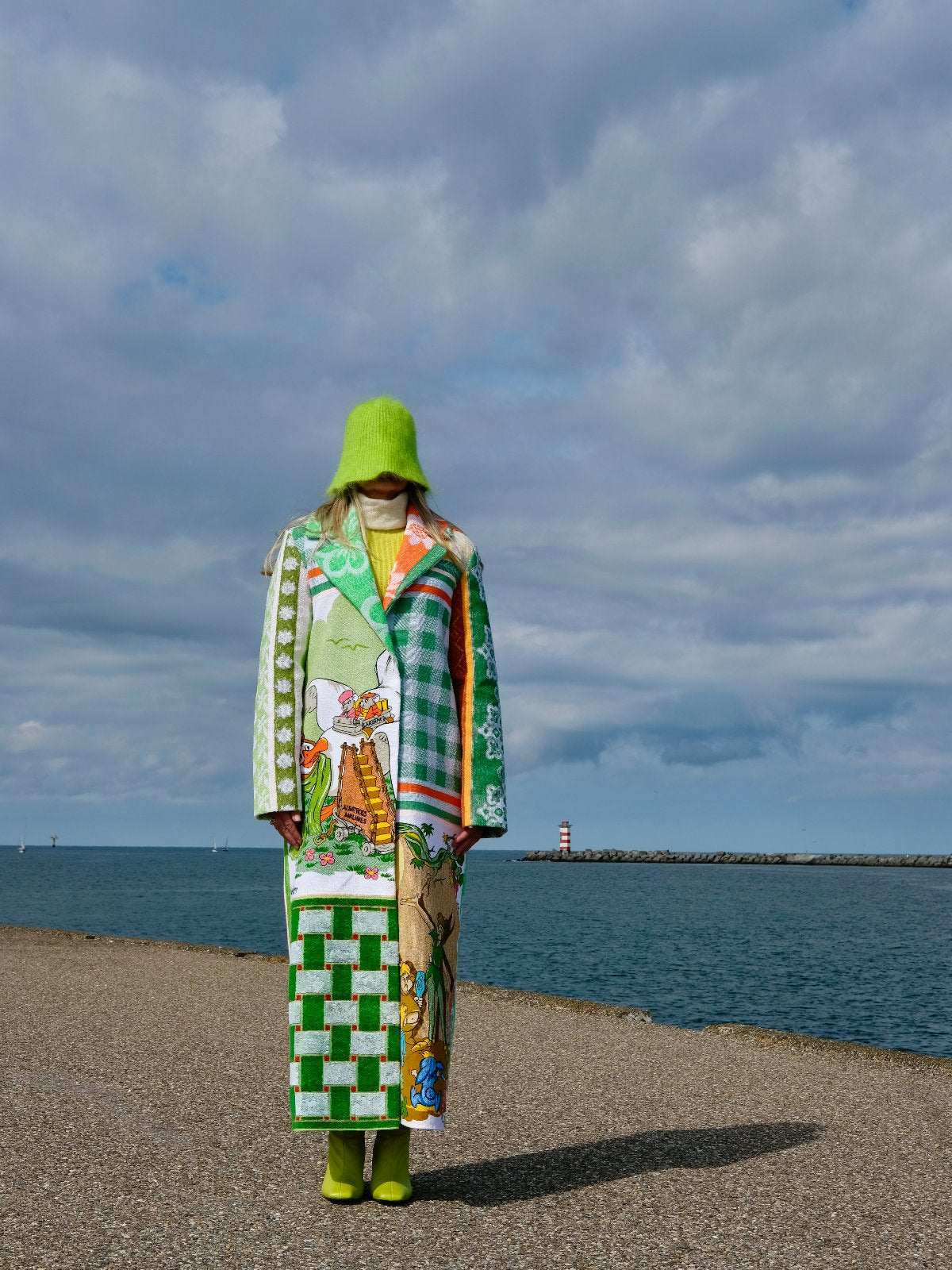 STUDIO WUNDERBAR Mouse With Big Ears Coat: green and orange patchwork long coat with gingham checks, floral motifs and a Mickey Mouse storybook panel, upcycled one-of-a-kind coat, worn by model, buy at DOORS NYC