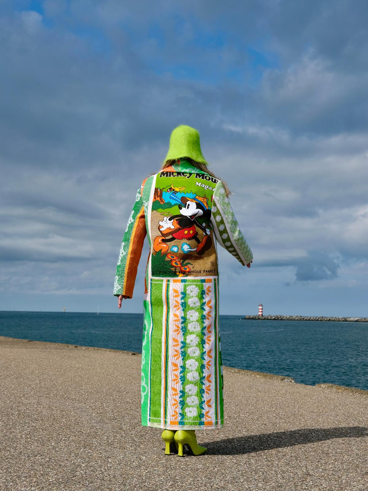 STUDIO WUNDERBAR Mouse With Big Ears Coat: green and orange patchwork long coat with gingham checks, floral motifs and a Mickey Mouse storybook panel, upcycled one-of-a-kind coat, worn by model, buy at DOORS NYC