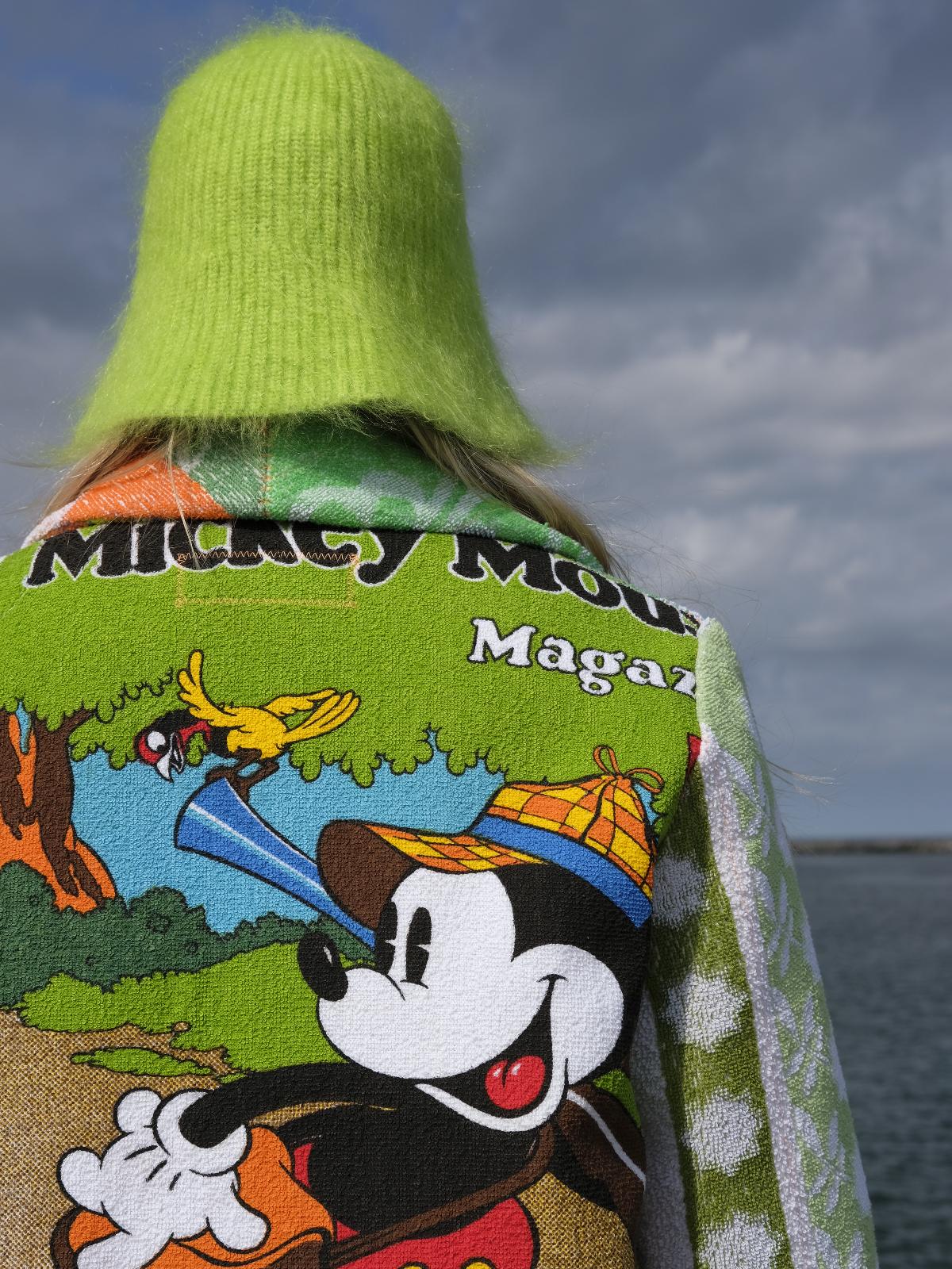 STUDIO WUNDERBAR Mouse With Big Ears Coat: green and orange patchwork long coat with gingham checks, floral motifs and a Mickey Mouse storybook panel, upcycled one-of-a-kind coat, worn by model, buy at DOORS NYC