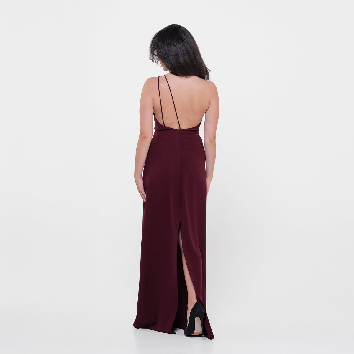 Woman wearing a burgundy evening gown with a slit on a white background