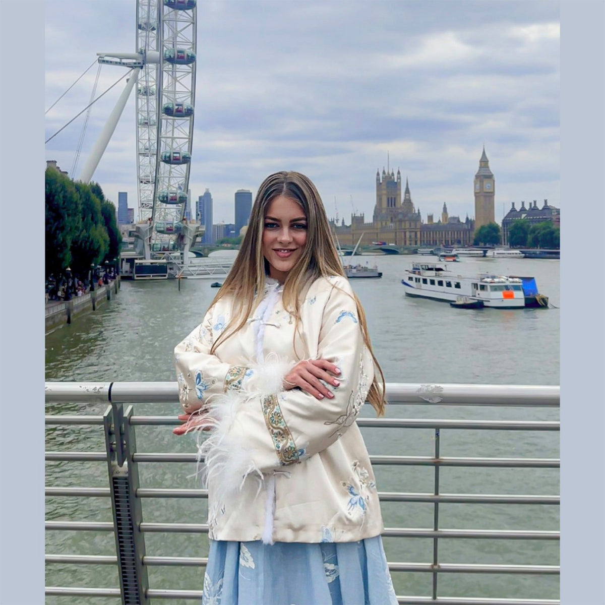 Woman in a white embroidered jacket standing in front of the London Eye and Big Ben.