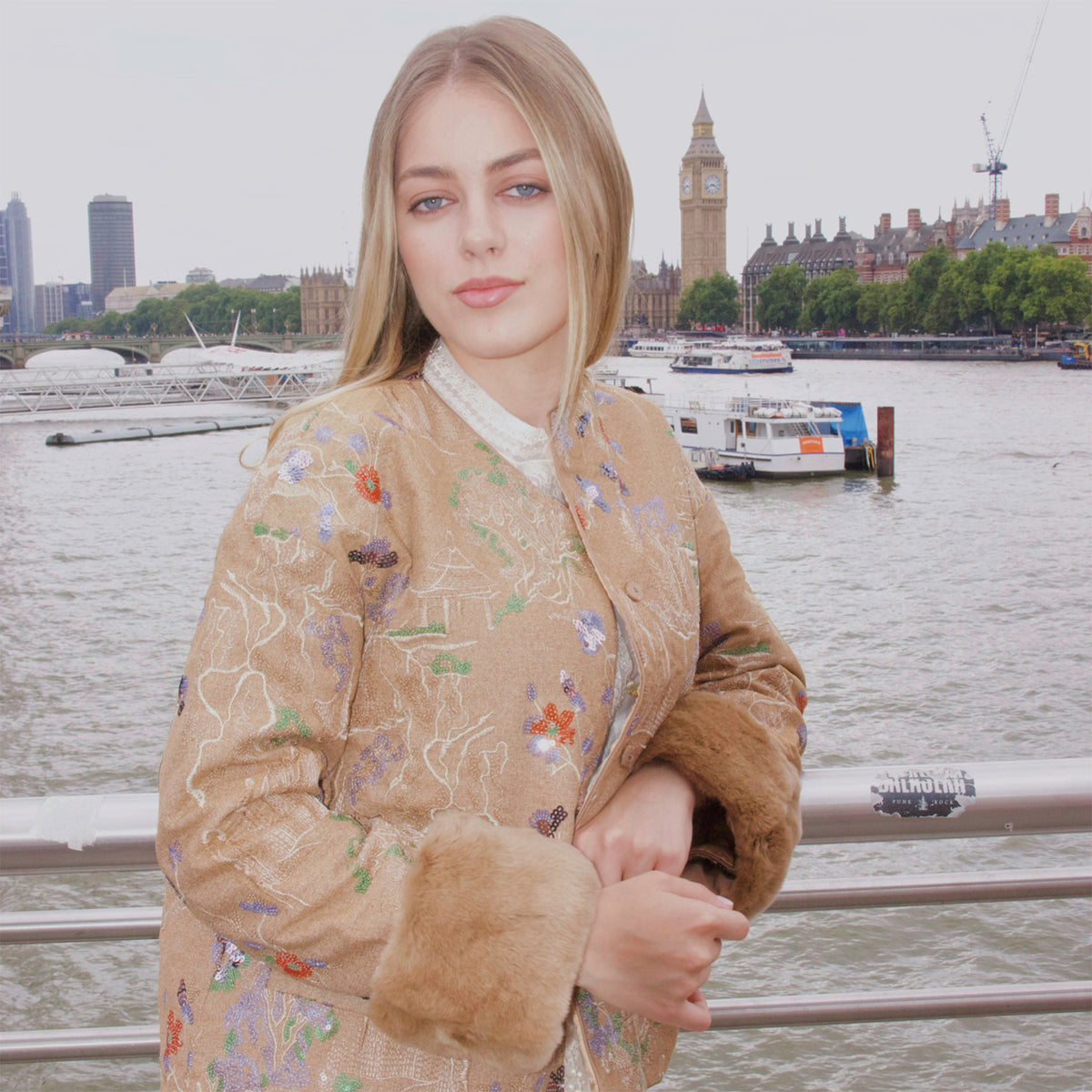 Woman in a patterned coat standing by a waterfront with Big Ben in the background