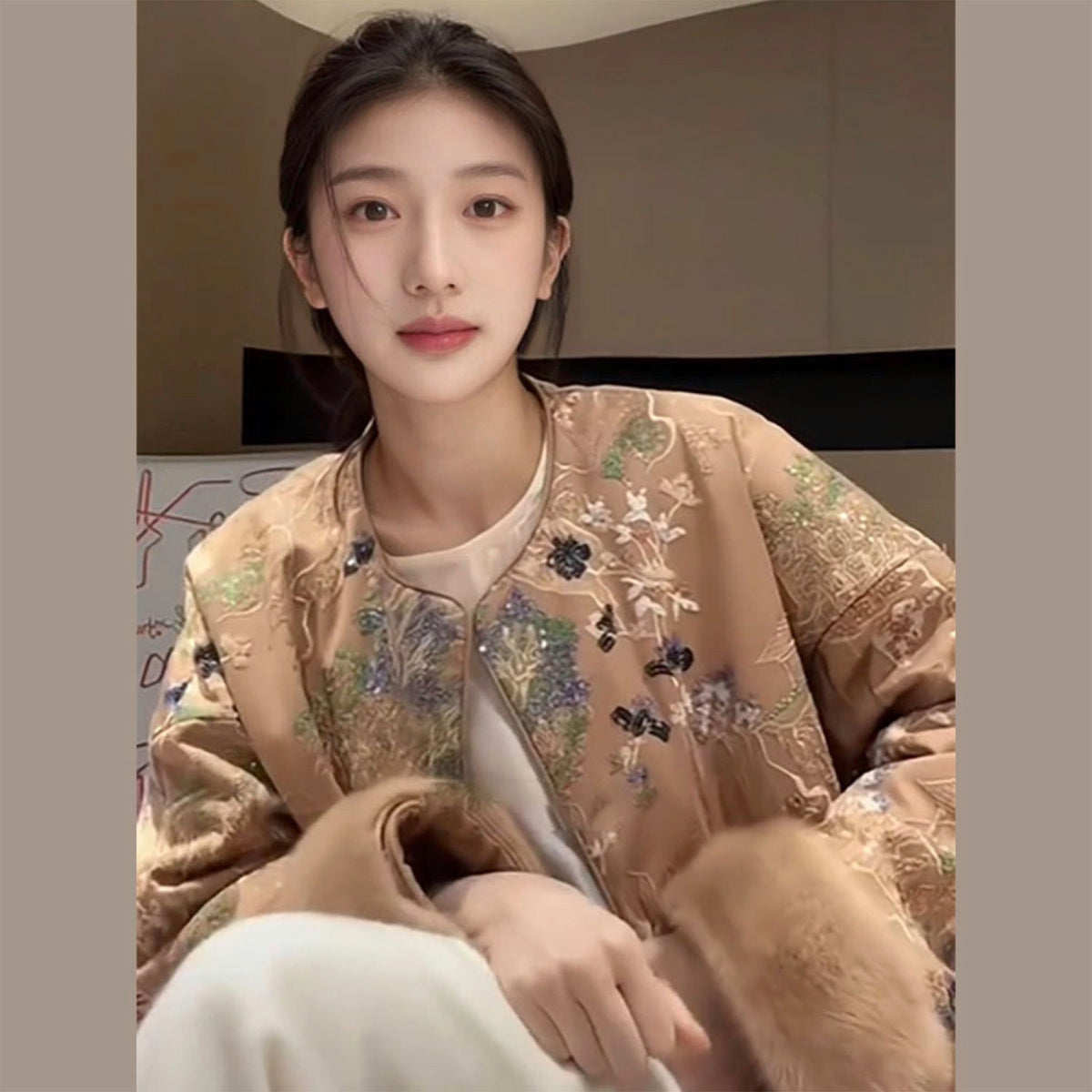 Woman wearing a beige embroidered jacket sitting indoors.