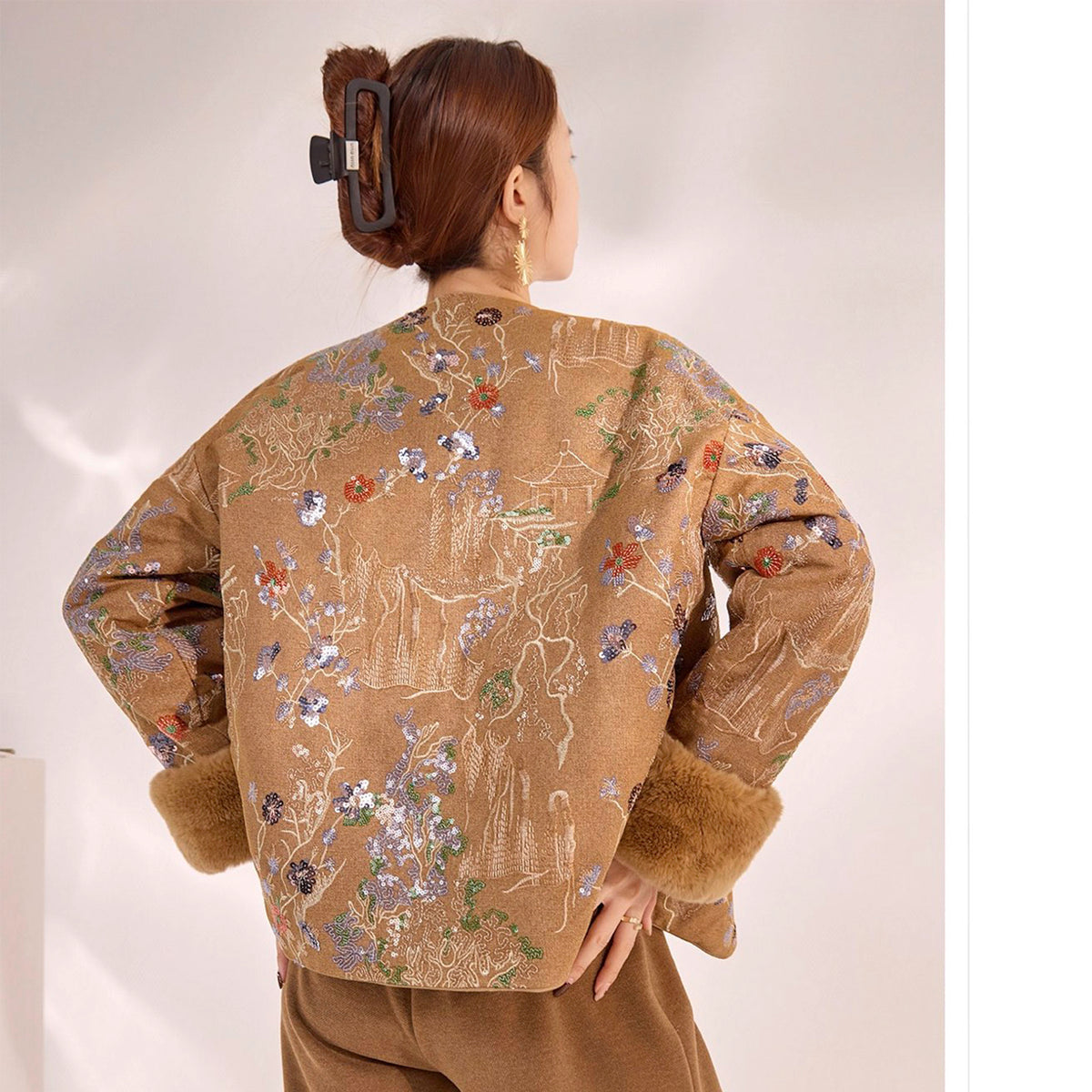 Person wearing a beige embroidered jacket with floral patterns on a plain background