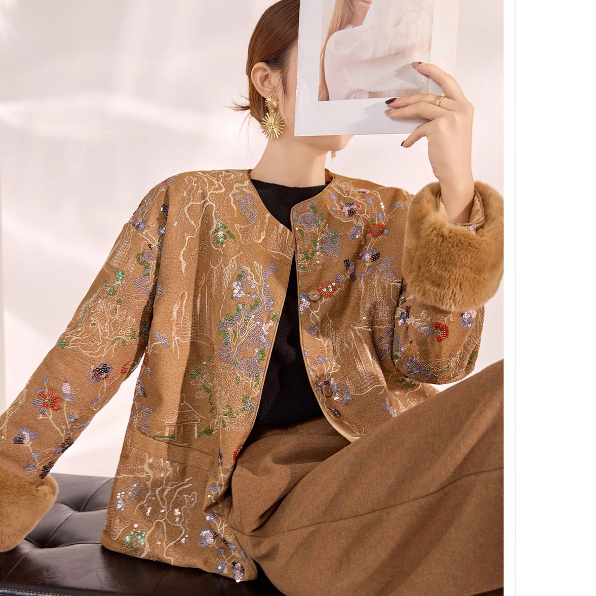 Person wearing a beige embroidered jacket with a neutral background