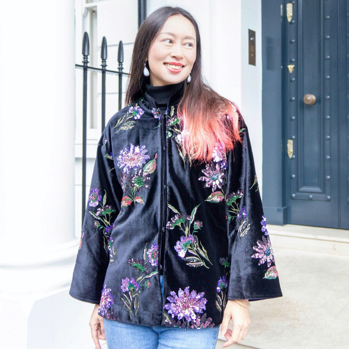 Woman wearing a black floral jacket standing in front of a building entrance.