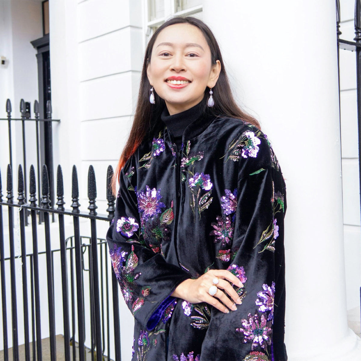 Woman wearing a black floral dress with purple accents standing in front of a white building.