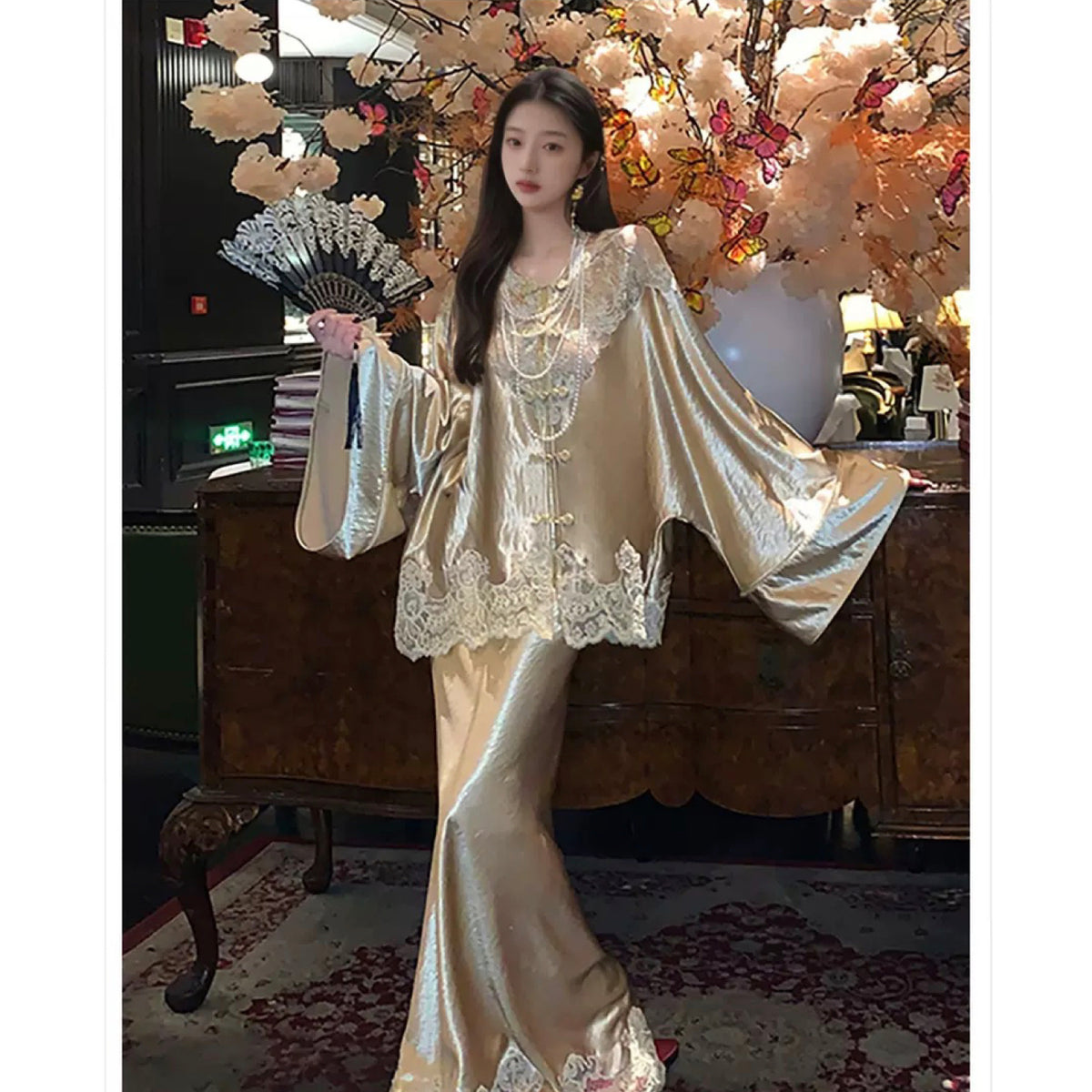 Woman in a luxurious outfit holding a fan in an elegant room with floral decorations.