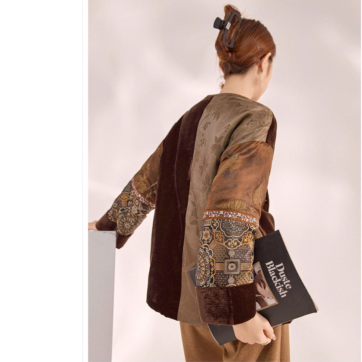 Mannequin wearing a brown and beige patterned outfit with a book titled &#39;Dust&#39; on a white background