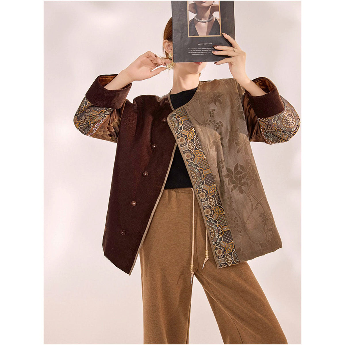 Person wearing a brown and gold embroidered jacket holding a book in front of their face.