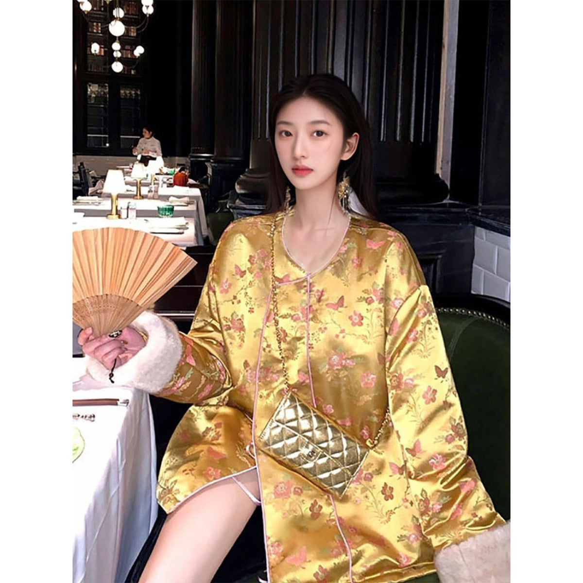 Woman in a gold traditional outfit holding a fan in an indoor setting