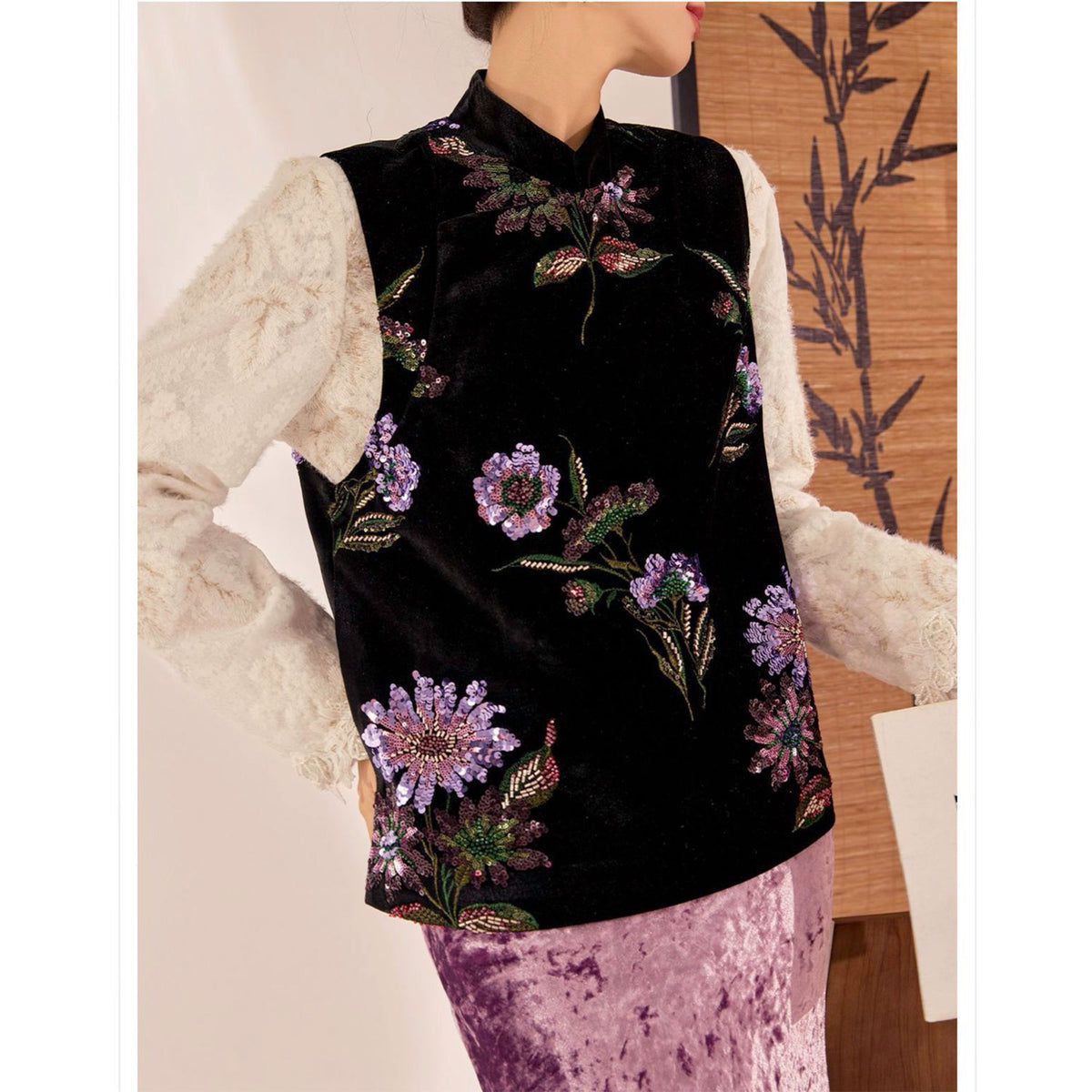 Mannequin wearing a black embroidered vest with floral patterns over a white lace top.