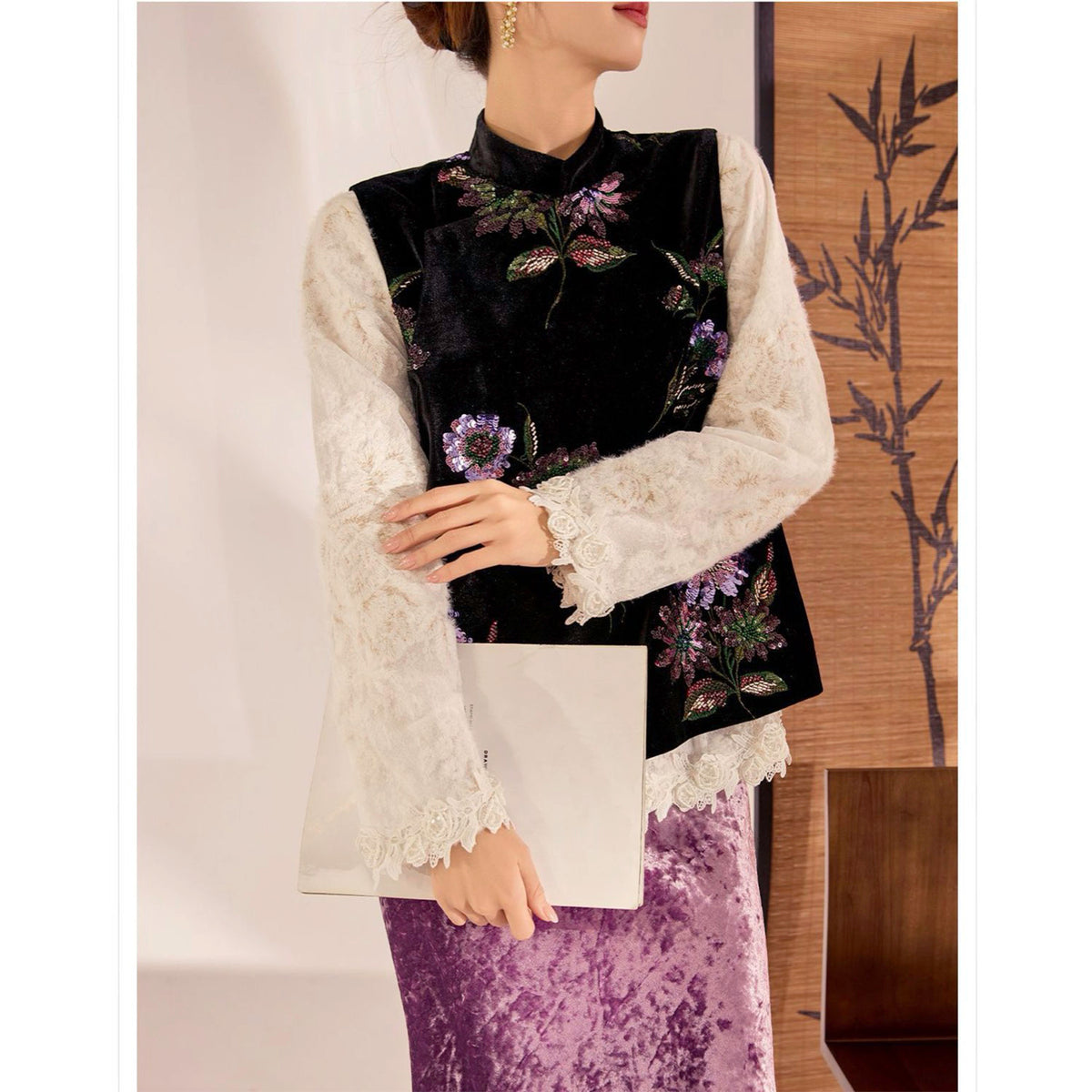 Woman wearing a black embroidered top with floral patterns, white lace sleeves, and a purple skirt.