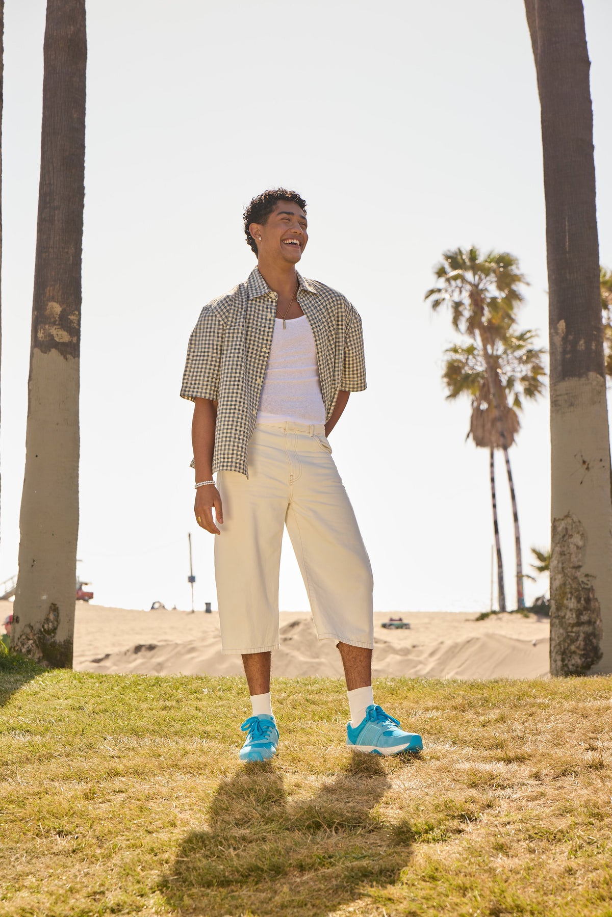 Person standing on grass with palm trees in the background wearing blue sneakers