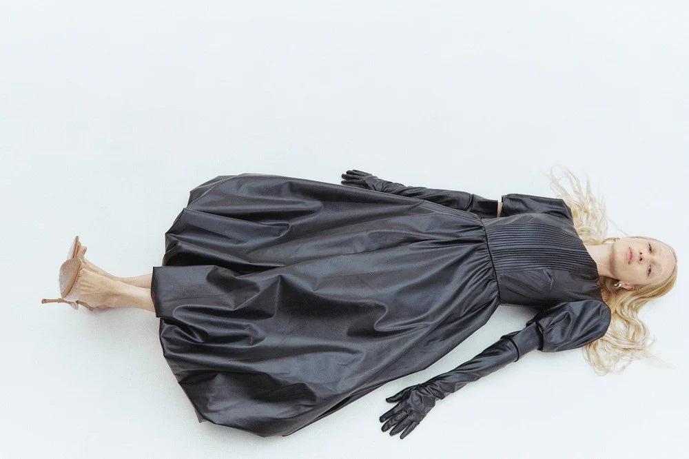 Person wearing a black dress and gloves lying on a white background