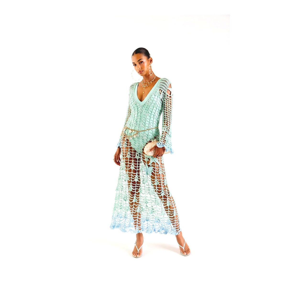 A woman models the ANDREEVA Aqua Marine Handmade Maxi Cover-Up Dress in light blue over matching pants, paired with a beige purse, strappy sandals, and gold jewelry against a white background.