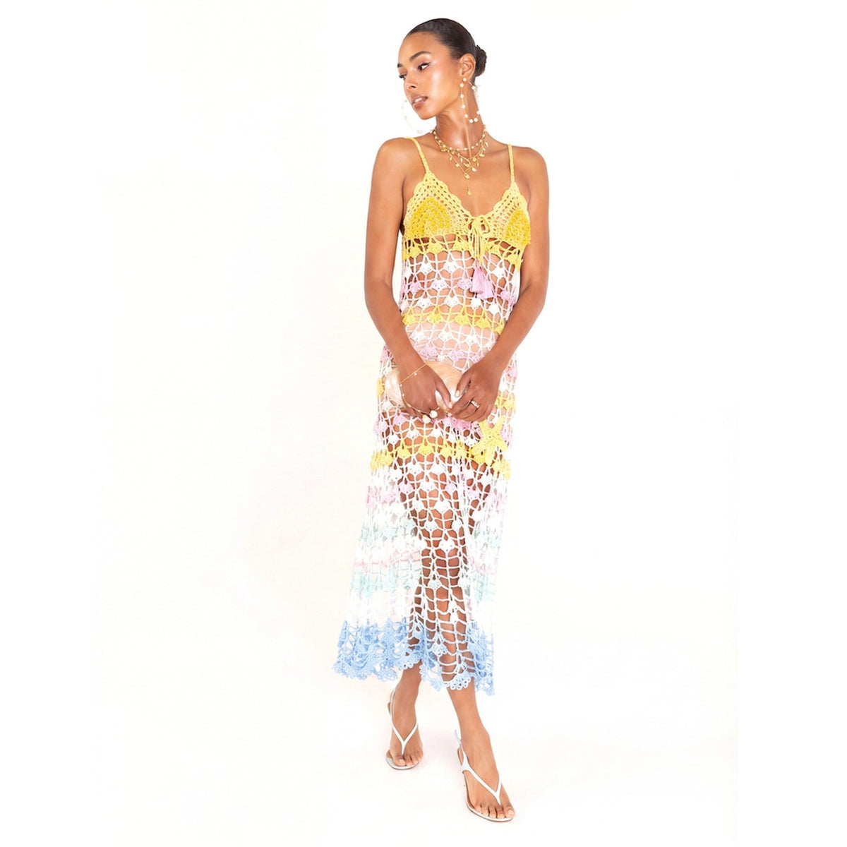 A woman models the ANDREEVA Flower Marine Handmade Maxi Crochet Dress, crafted from mercerized Brazilian cotton with yellow, white, pink, and blue floral crochet patterns, styled with layered necklaces, earrings, and strappy sandals against a white background.