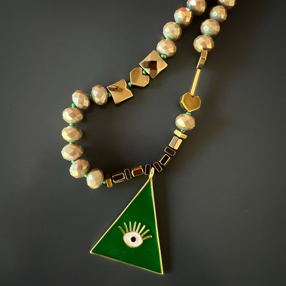 the Green Evil Eye Unique Necklace, highlighting the intricate craftsmanship of the pendant and the delicate arrangement of the green and beige crystal beads, gold hematite stone heart shape beads, and Alhambra flower beads. 