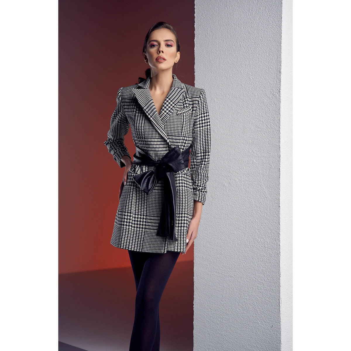 Woman wearing a checkered coat with a belt against a plain background