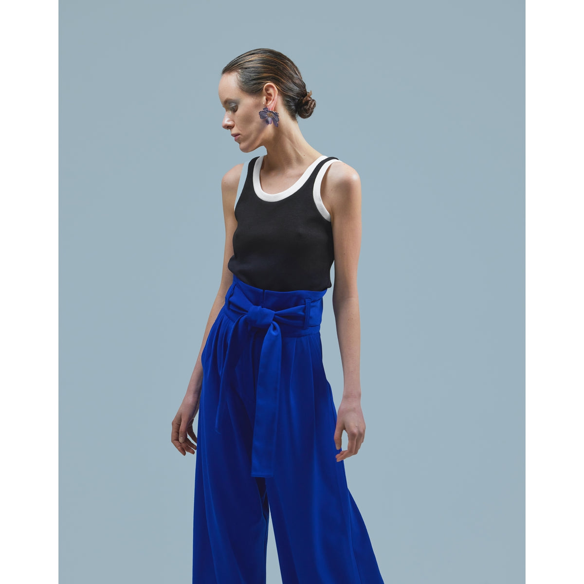 A person with slicked-back hair wears a sleeveless black top with white trim and JULIA ALLERT Blue High Waist Long Wide Leg Trousers tied with a sash, standing against a light blue background.