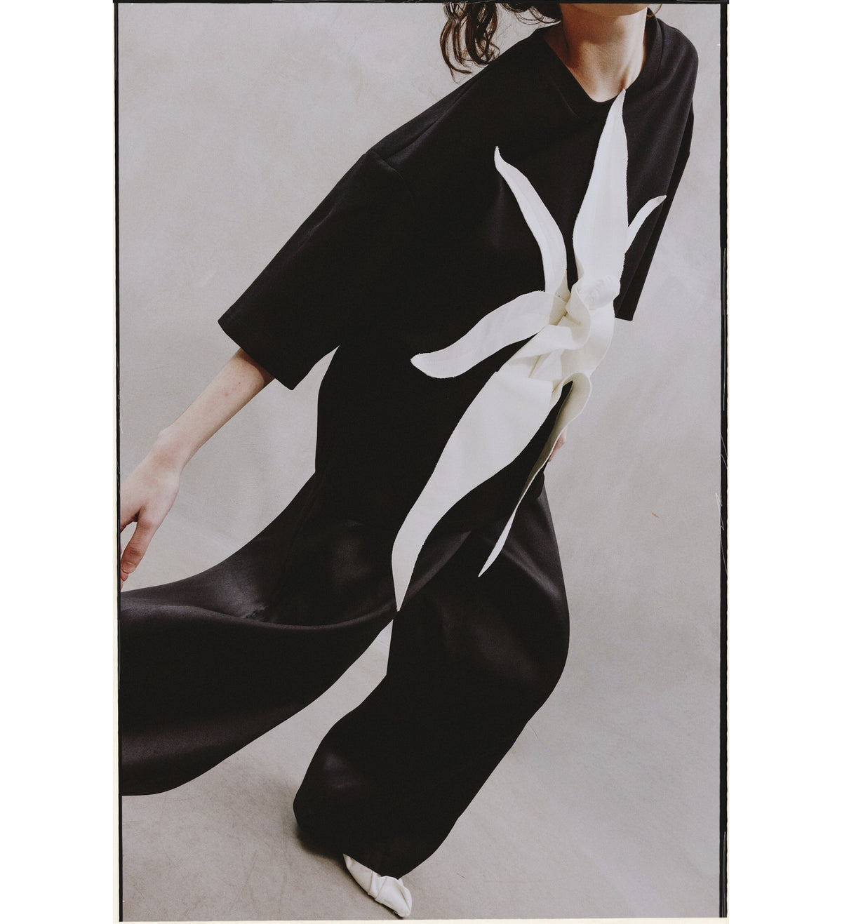 An individual poses dynamically in the Relaxed Fit Knit Top - Black by JULIA ALLERT, featuring a bold, sculptural floral appliqué across the front, set against a light neutral background.