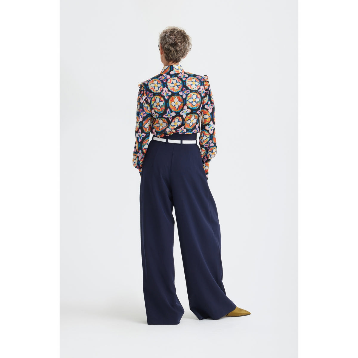 A person faces away, wearing JULIA ALLERT’s Fashion Forward Wide-Leg Pants &amp; Contrast Belt in navy, paired with mustard shoes and a colorful, circular-patterned blouse. Background is plain white.