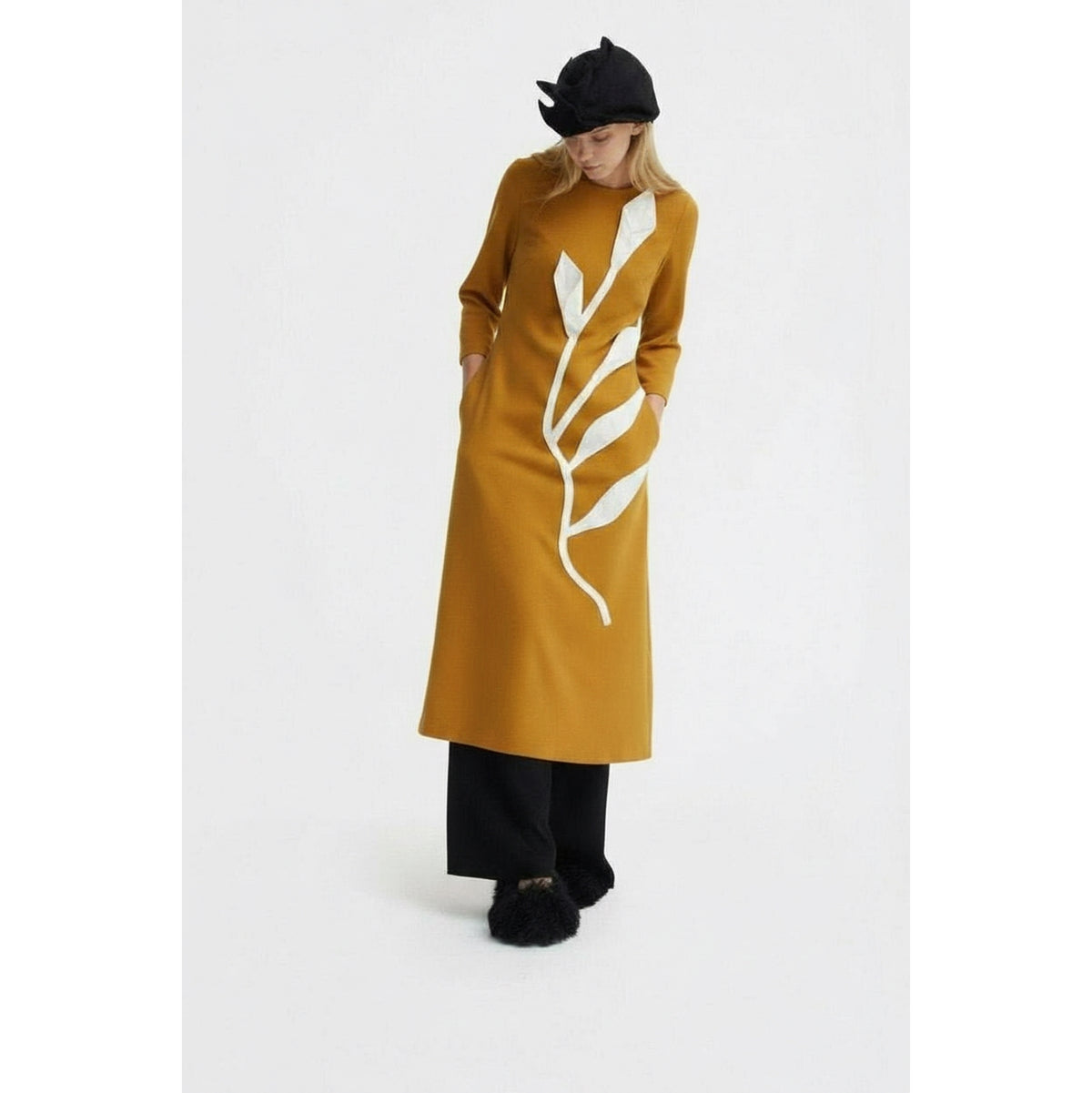 A woman in a JULIA ALLERT Art-Inspired Semi-Fitted Three-Quarter Sleeves Dress - Mustard stands against a plain background, styled with black wide-leg pants, furry-accented black shoes, and a chic black hat.