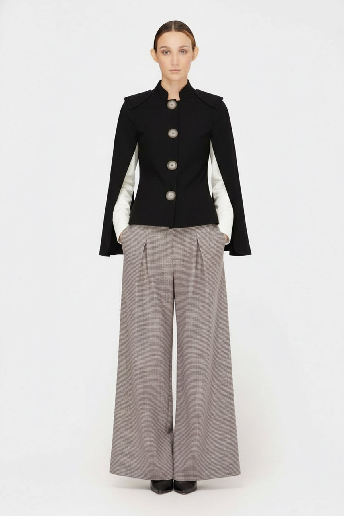 A woman faces forward, wearing the JULIA ALLERT Tailored Structured Cape Blazer in black over a white shirt and wide-legged gray trousers, set against a plain white background.