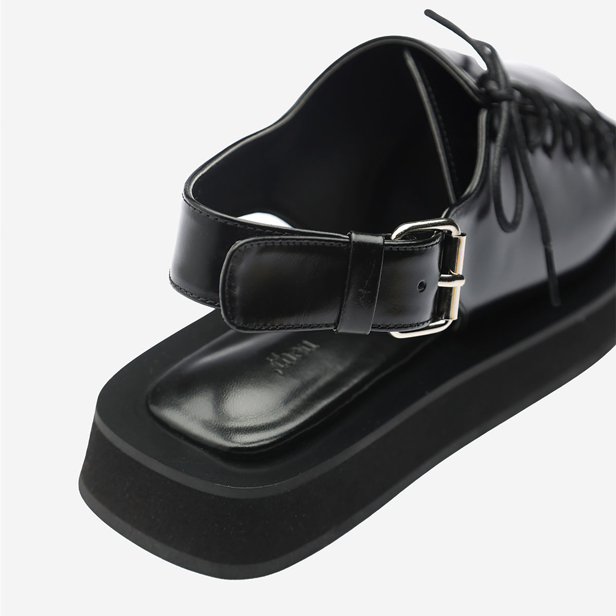 Close-up of THEN Black Leather Lace-Front Slingback Sandals, handcrafted in Korea with a thick sole, square toe, ankle strap with silver buckle, and lace-up upper detailing, photographed against a white background.