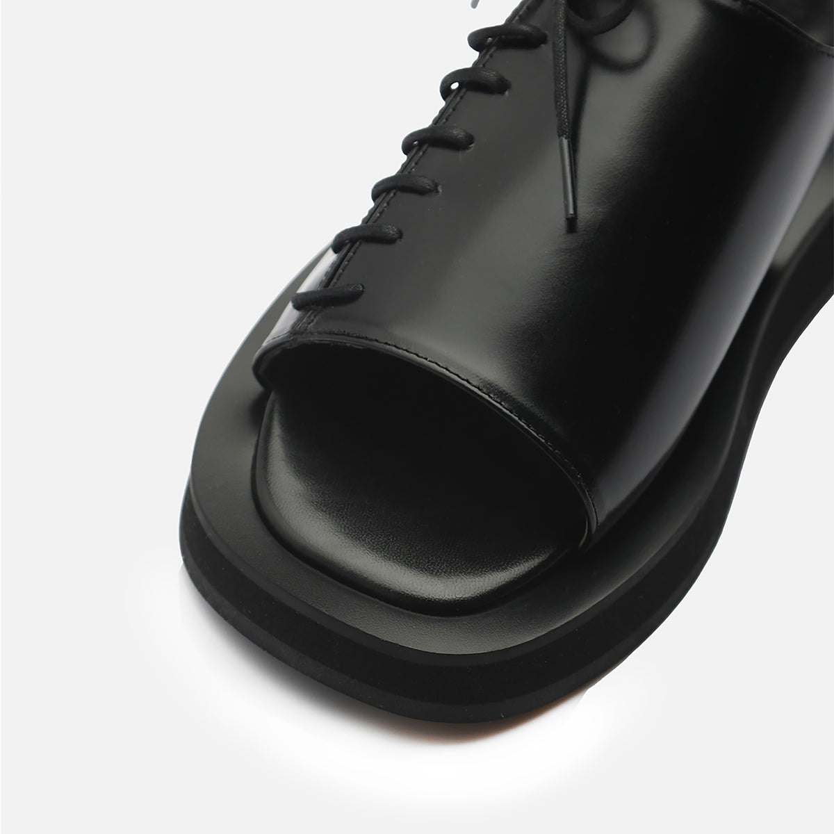 Close-up of THEN Black Leather Lace‑Front Slingback Sandals, handcrafted in Korea with a shiny finish, open square toe, and thick rectangular sole on a light background.