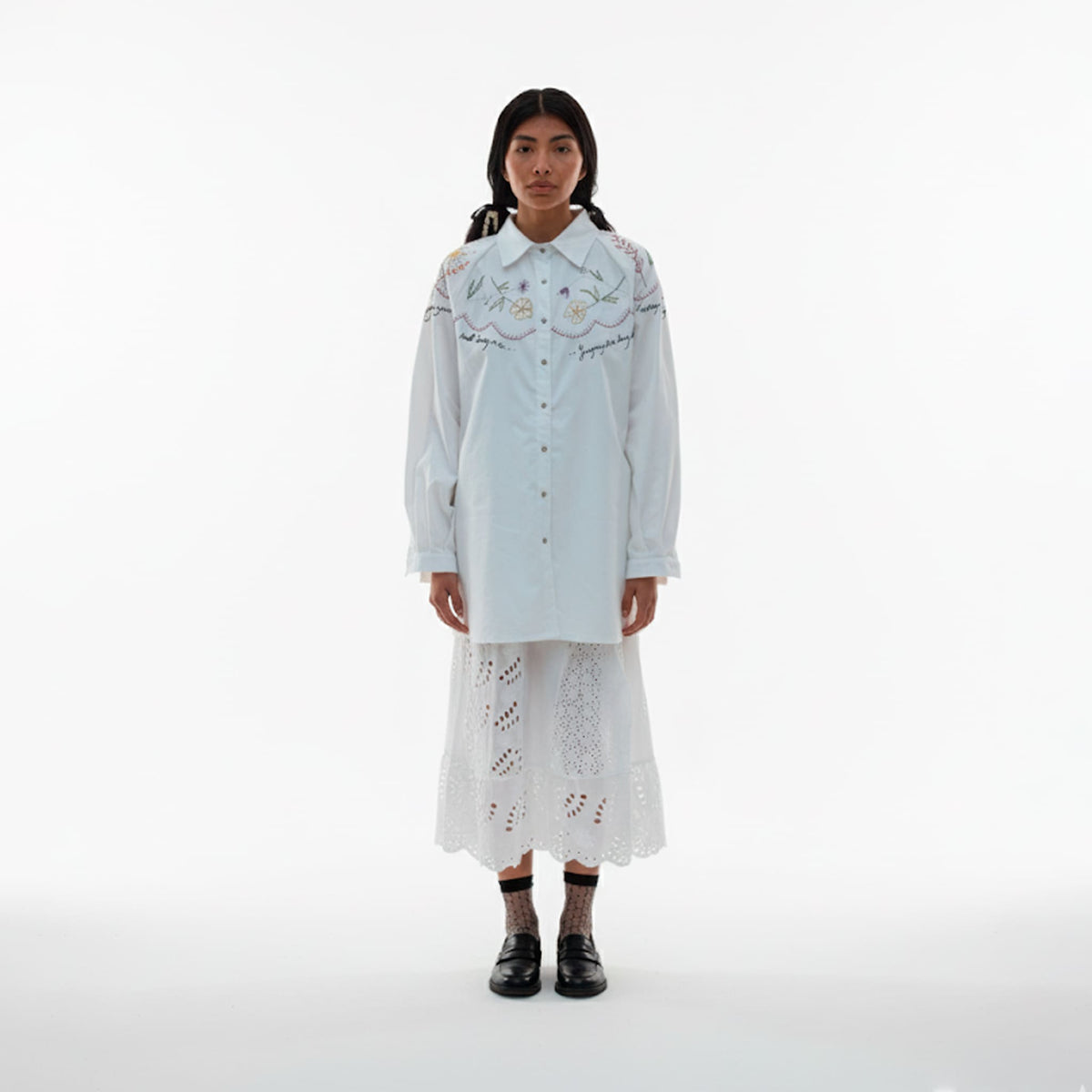 Person wearing a light blue embroidered shirt and white lace skirt on a white background