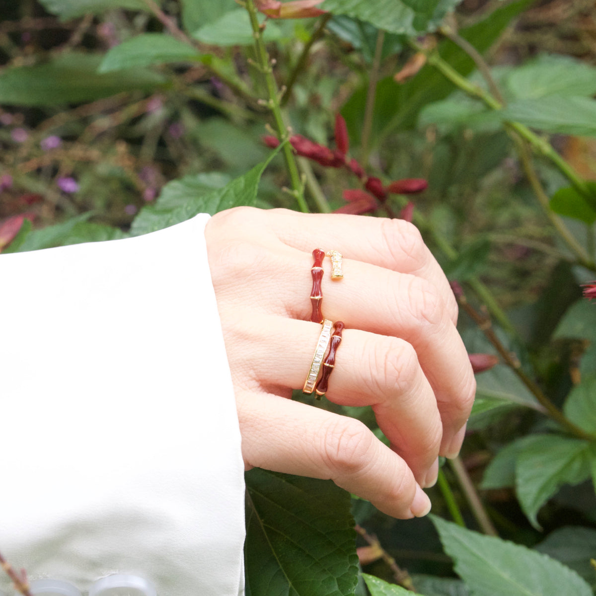 Hand wearing two rings with a natural background of green leaves and red flowers