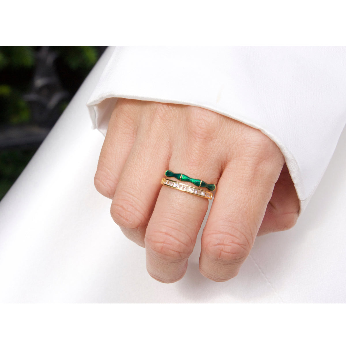 Hand wearing a gold ring with green gemstones on a white background