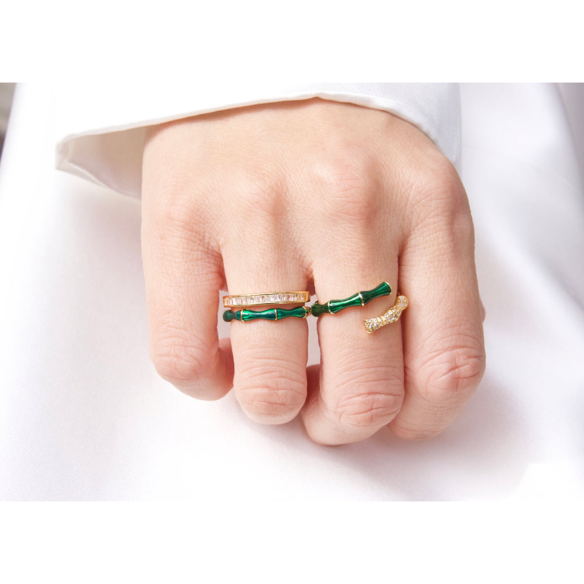 Hand wearing two green and gold rings on a white background
